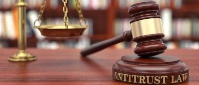 un martelletto da giudice appoggiato su un supporto dove è scritto "antitrust", e una bilancia su una scrivania
